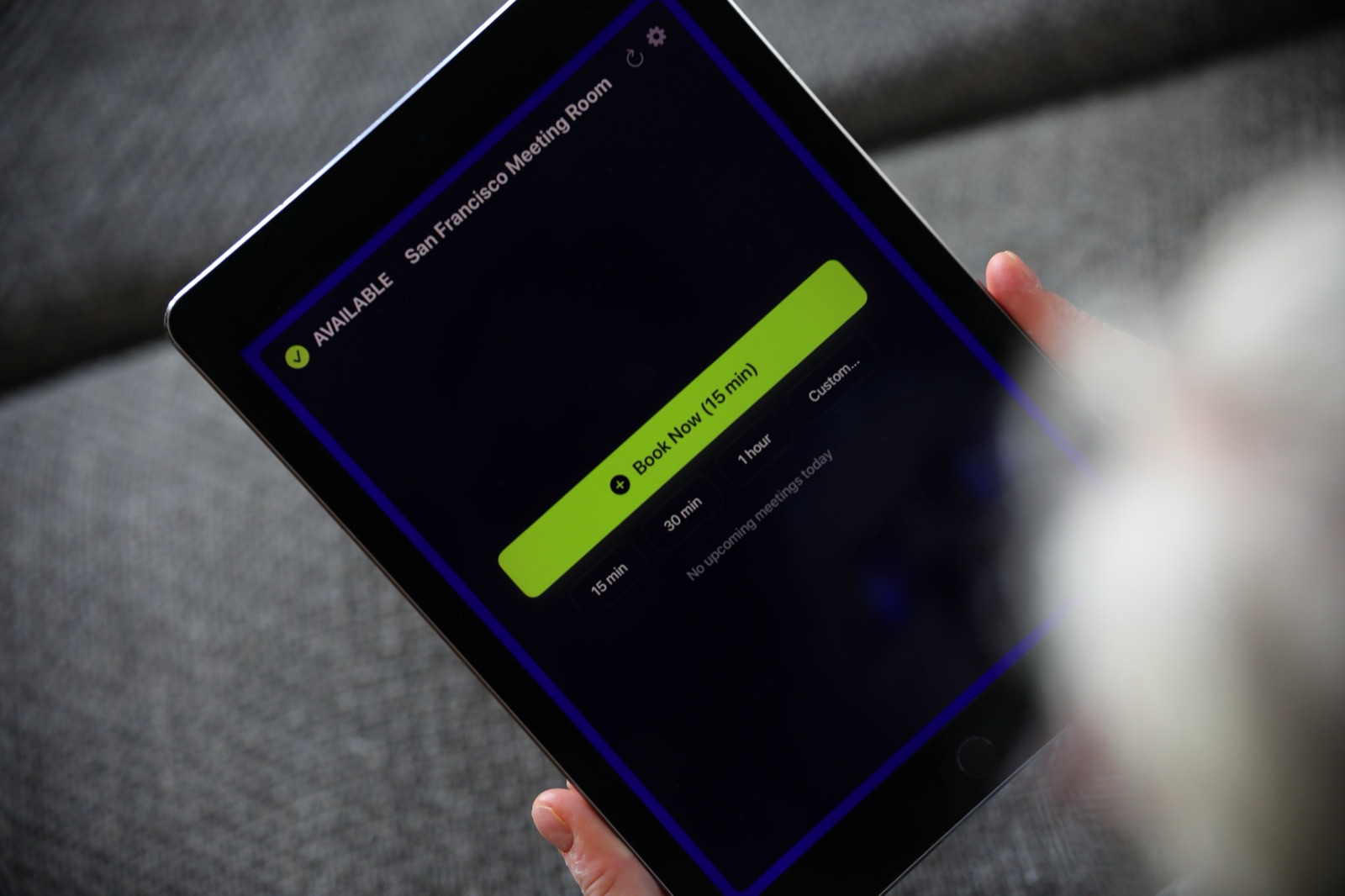 L'application The Room Display fonctionnant sur un iPad tenu à la main, affichant une salle disponible
